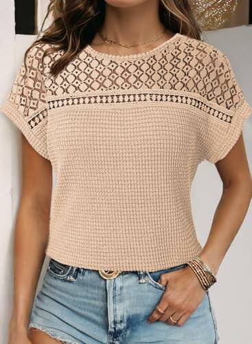 Woman wearing a beige crochet top with denim shorts.