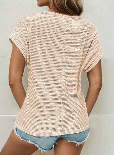 Person wearing a beige knit top and denim shorts, seen from the back.