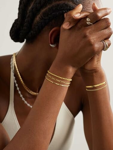 Person wearing stacked gold bracelets and necklaces.