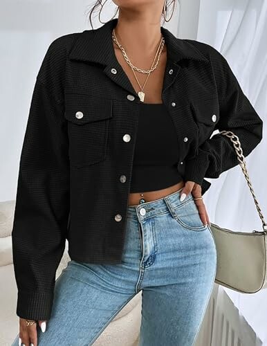 Woman wearing a black jacket and jeans, accessorized with necklaces and a handbag.