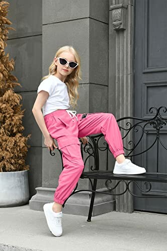 Girl in pink pants and sunglasses sitting on a bench.