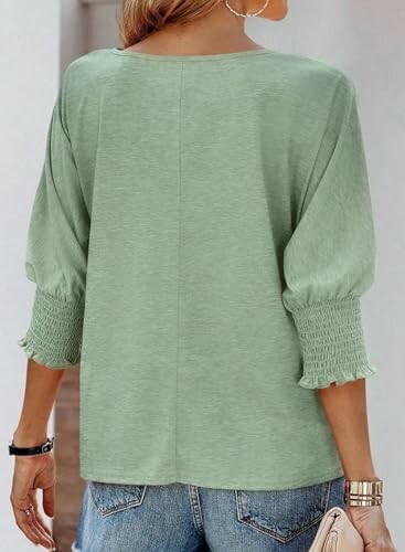 Woman in green blouse with puff sleeves and jeans, back view.