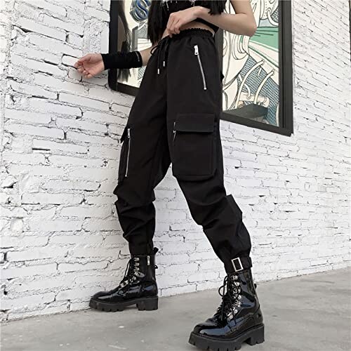 Person wearing black cargo pants and boots against a white brick wall.