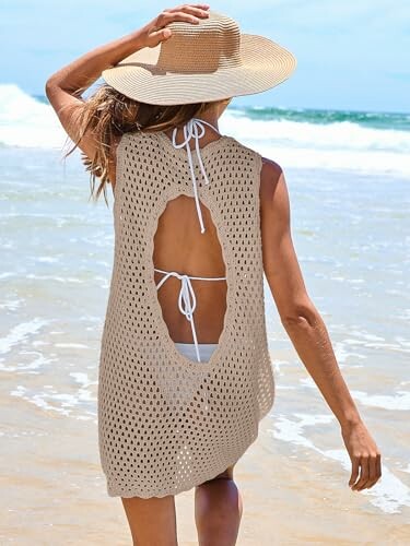 Woman in crochet beach cover-up and hat walking on the beach.