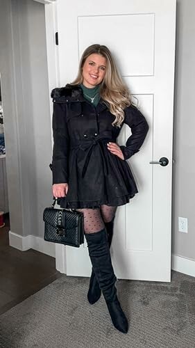 Woman in black coat and boots standing indoors.