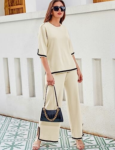 Woman in cream outfit with black trim holding a handbag.