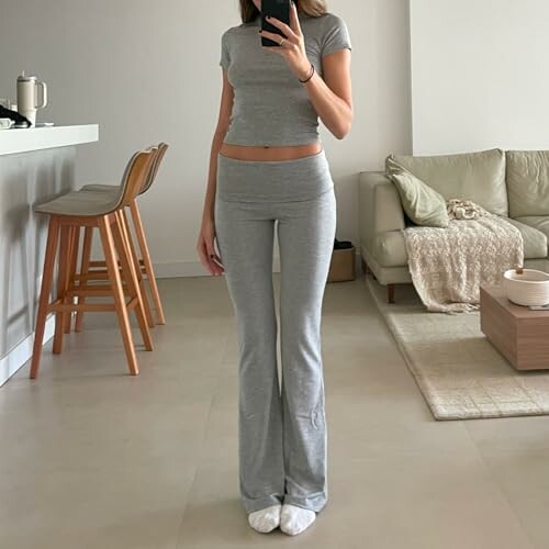 Woman in grey loungewear taking a mirror selfie in a modern living room.