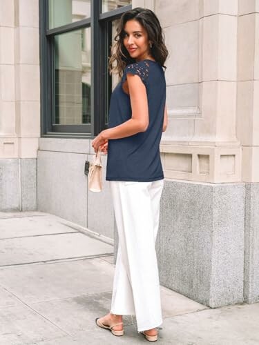 Woman in navy top and white pants standing on a city sidewalk.