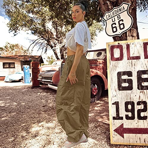 Woman in casual outfit standing near Route 66 sign with vintage cars