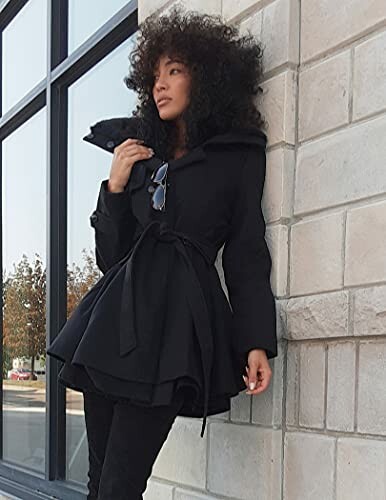 Woman with curly hair wearing a black coat standing by a building