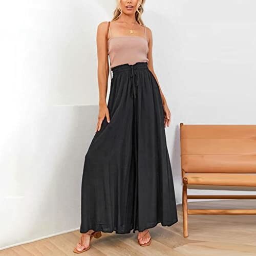 Woman in black wide-leg pants and beige top standing indoors.