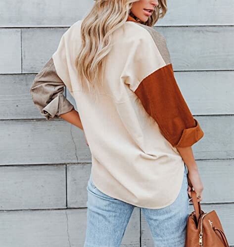 Woman in a colorblock shirt and jeans holding a brown handbag.