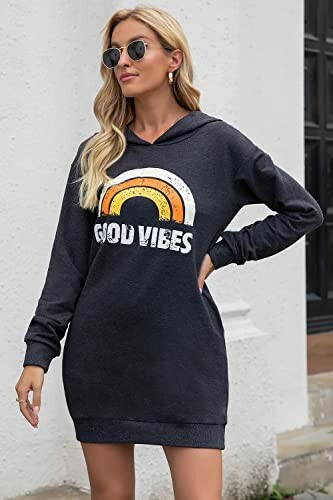 A woman in a dark hoodie dress with 'Good Vibes' text and rainbow design.