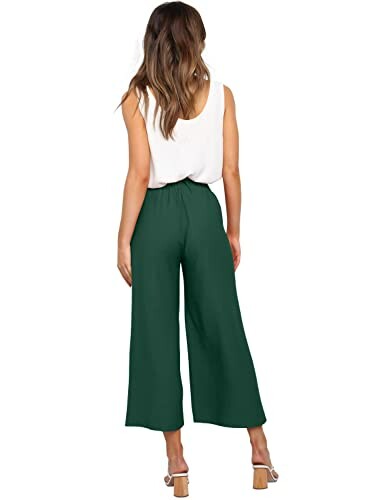 Woman in white top and green wide-leg pants, back view.