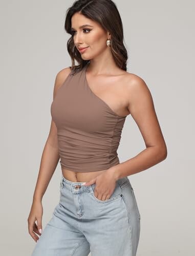 Woman in a one-shoulder brown top and light jeans.