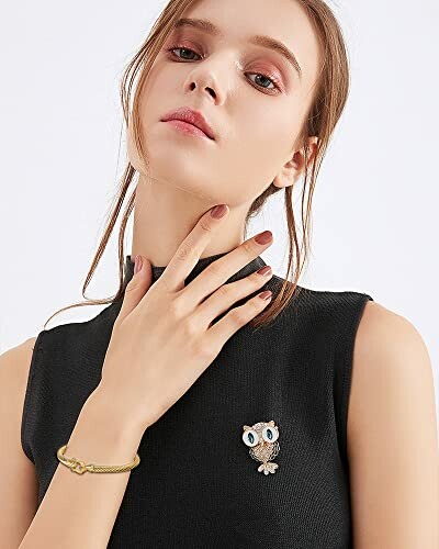 Woman in black top wearing an owl brooch and bracelet.