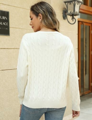 Woman in white sweater standing outside near a building.