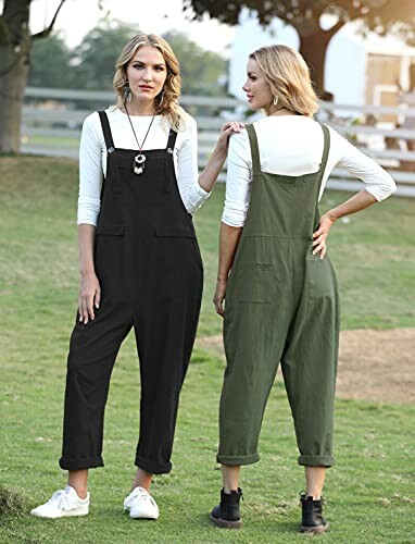 Two women in overalls standing on grass.